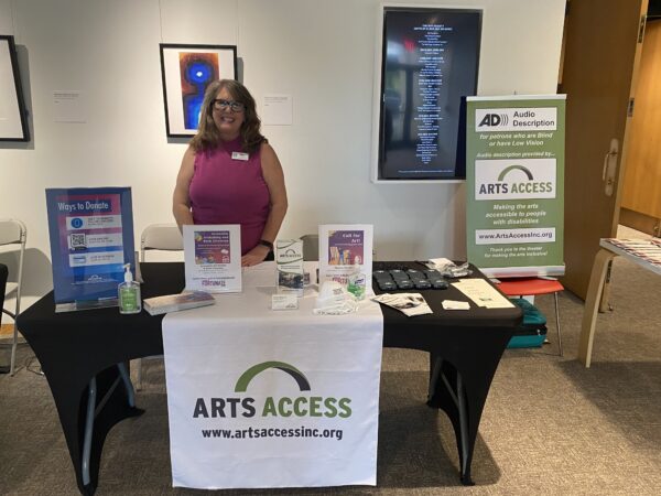 Eileen Bagnall standing with the Arts Access info table at an event.